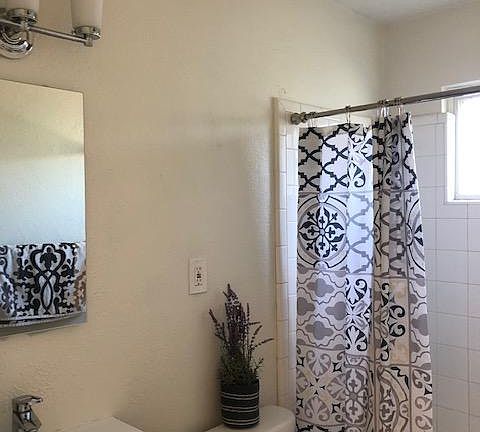 Remodeled bath has black shaker vanity with integrated porcelain sink, medicine cabinet, LED lighting, white tile tub/shower surround, gray tile floors, window for natural light