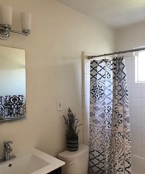 Remodeled bath has black shaker vanity with integrated porcelain sink, medicine cabinet, LED lighting, white tile tub/shower surround, gray tile floors, window for natural light