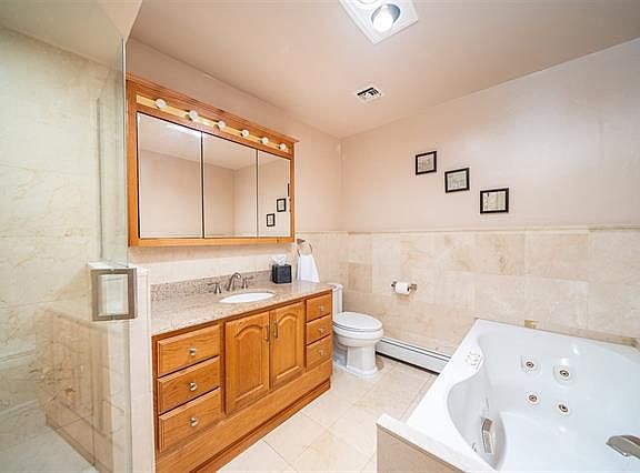 Elegant bath with marble tiles, jacuzzi, glass shower, and wood vanity. Spa-like feel with soft lighting and premium finishes.