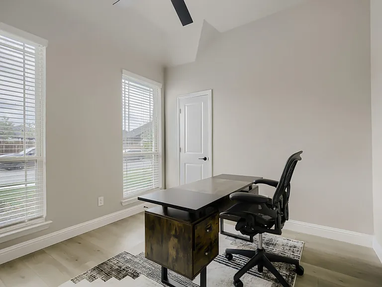 Office featuring two large windows with blinds, light wood-finish flooring, and a vaulted ceiling
