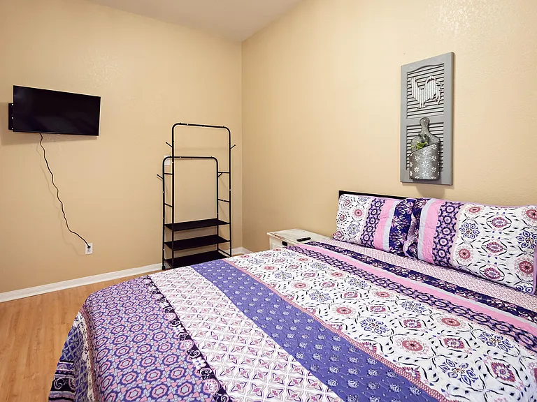 Furnished bedroom with a comfortable bed, wall-mounted TV, nightstand, and open shelving for convenient storage.