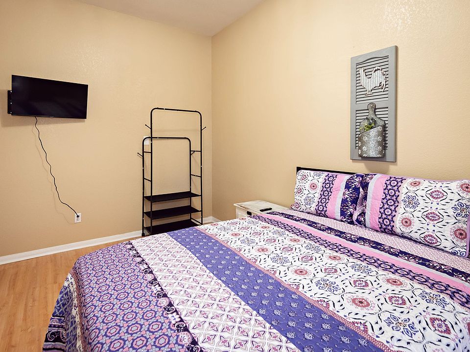 Furnished bedroom with a comfortable bed, wall-mounted TV, nightstand, and open shelving for convenient storage.