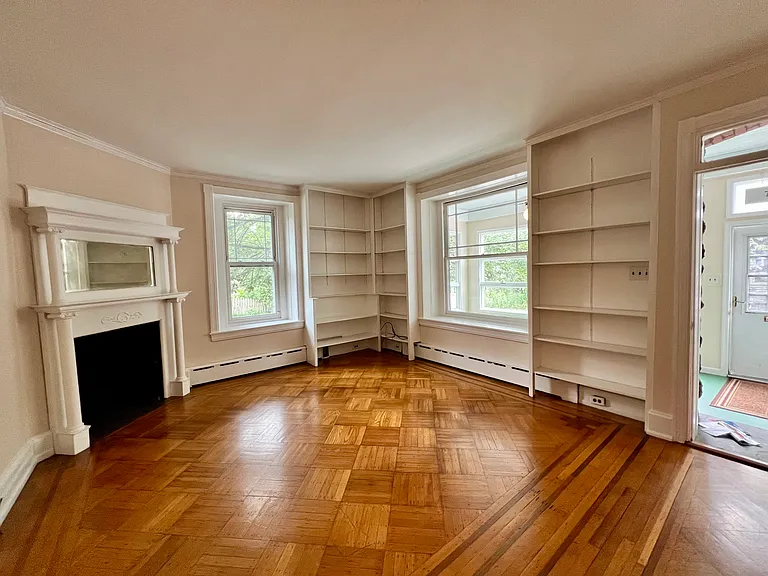 Living room with bookcases, parquet floors and a decorative fireplace.