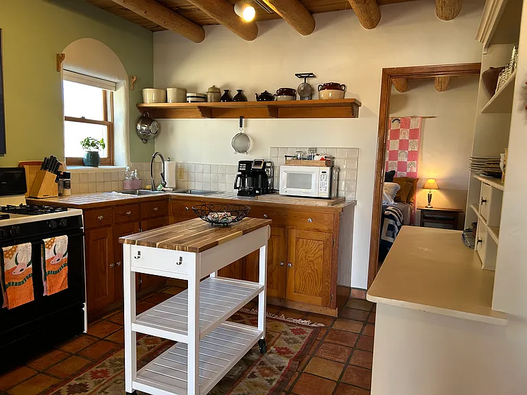 Nambe Casita kitchen with rolling kitchen island looking towards the bedroom. Kitchen has separate under-counter refrigerator and freezer and gas stove.