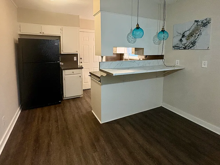 Open Living & Dining Area
spacious layout with wood-look flooring
Kitchen black refrigerator, white cabinetry, and countertop bar
Breakfast Bar -marble-look countertop with seating space
Pendant Lighting -stylish blue glass hanging lights