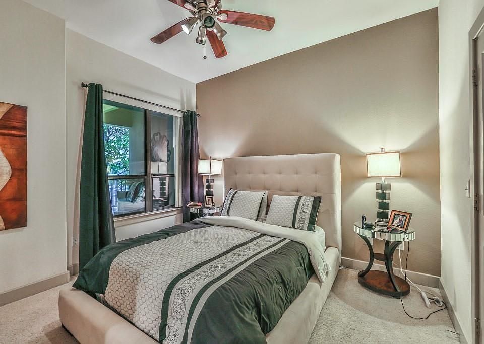 Tranquil bedroom retreat with plush carpeting, high ceilings, and natural light streaming through large windows. A ceiling fan adds comfort, while neutral tones create a serene and restful atmosphere.
