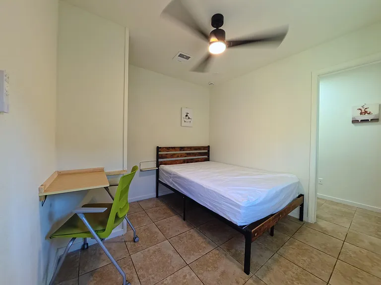Furnished bedroom with ceiling fan, tiled floors, and a built-in desk area for work or study.