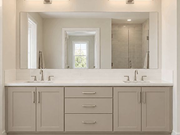 A double vanity with a wide mirror, two rectangular wall lights, and white countertops above light-g