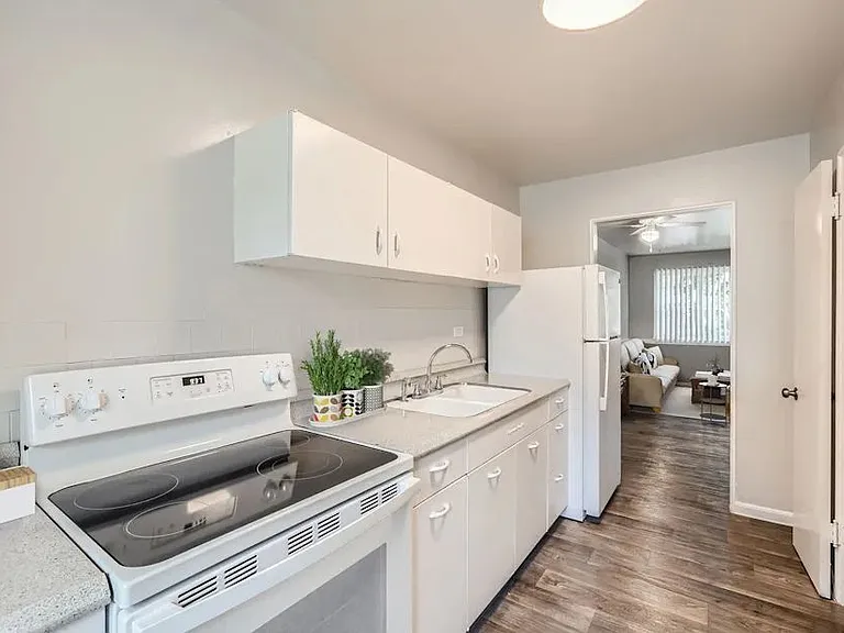 A white kitchen with a stove, sink, and cabinets.