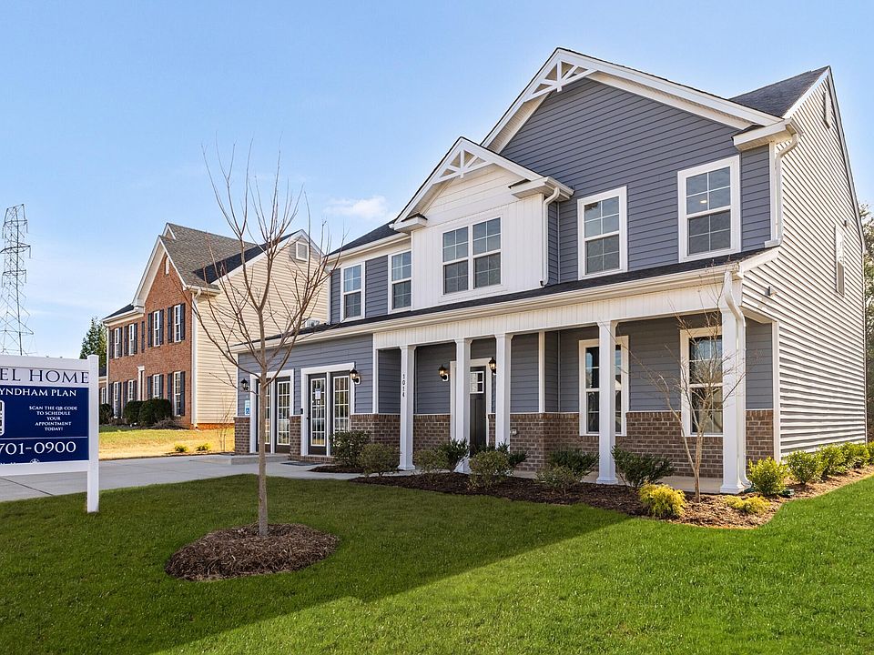 A modern two-story model home with gray siding, white trim, a covered porch, and well-kept landscapi