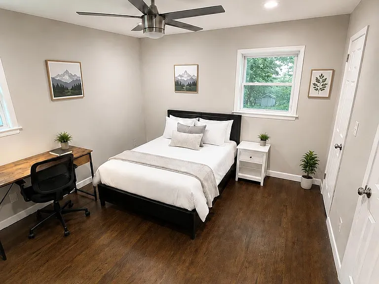 Furnished bedroom with hardwood floors, ceiling fan, work desk, and a window for natural light plus nightstand storage.