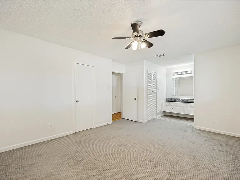 Spacious carpeted room featuring a ceiling fan with light fixture, window with blinds, and white painted walls