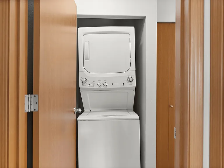 Compact laundry area with a modern stackable washer and dryer set, neatly integrated into a closet space with wooden doors. Compact laundry area with a modern stackable washer and dryer set, neatly integrated into a closet space with wooden doors.