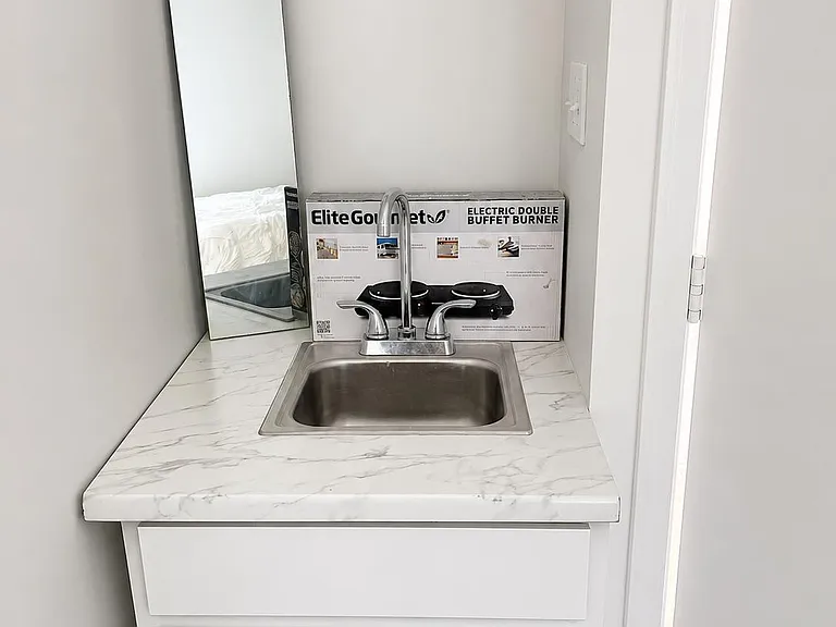 Minimalist kitchenette nook with stainless sink, marble-look countertop, and base cabinet storage for everyday convenience.