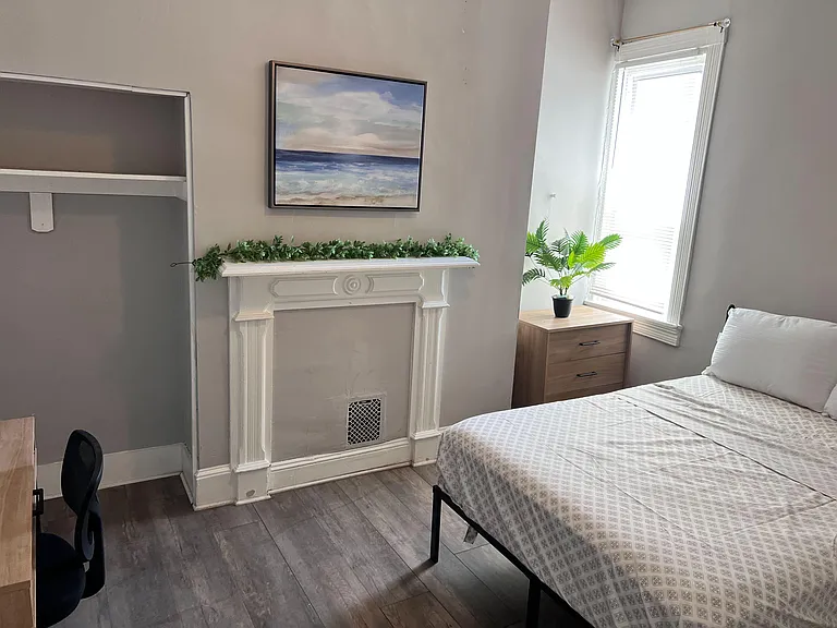 Bedroom featuring a decorative fireplace mantel, closet shelving, and a window with blinds for natural light.