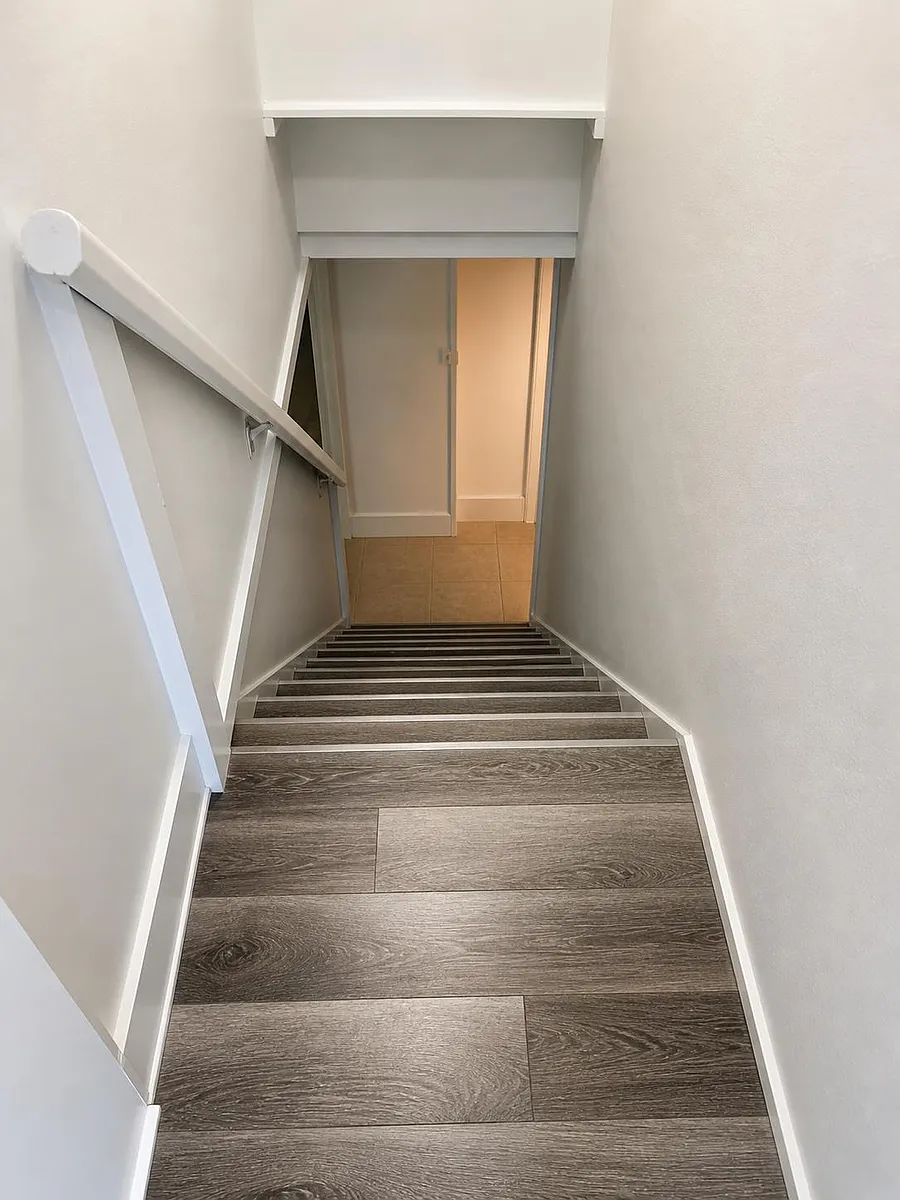 Clean stairwell with wood-look flooring, sturdy handrail, and direct access to the lower-level hallway. - Garfield St