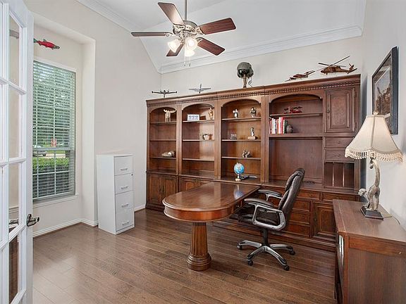 Private home office with double crown molding, ceiling fan, hardwood flooring and french doors is located just off the entry.