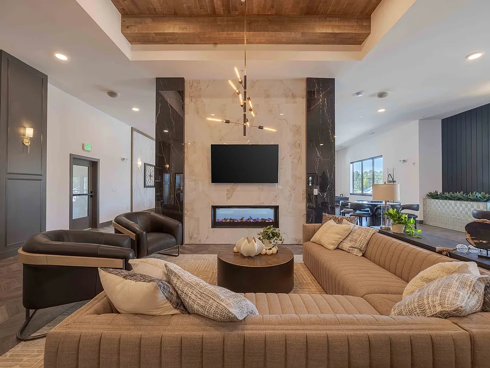Leather accent chairs and a sectional sofa surround a linear gas fireplace in the clubhouse lounge, giving residents a quiet spot to relax near the game and kitchen areas.
