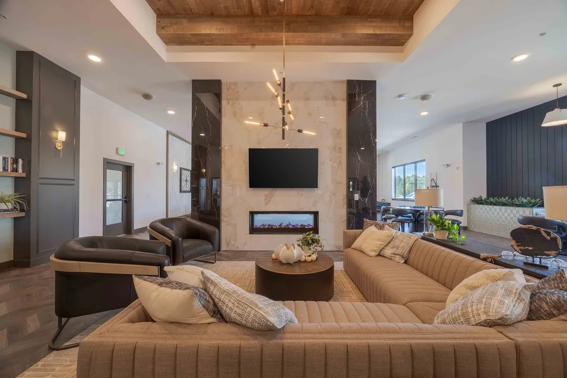 Leather accent chairs and a sectional sofa surround a linear gas fireplace in the clubhouse lounge, giving residents a quiet spot to relax near the game and kitchen areas.