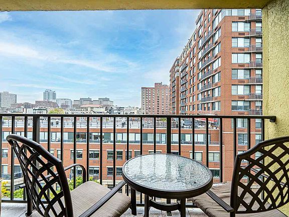 Balcony with round glass table, two chairs, and city views of modern apartment buildings in the background.