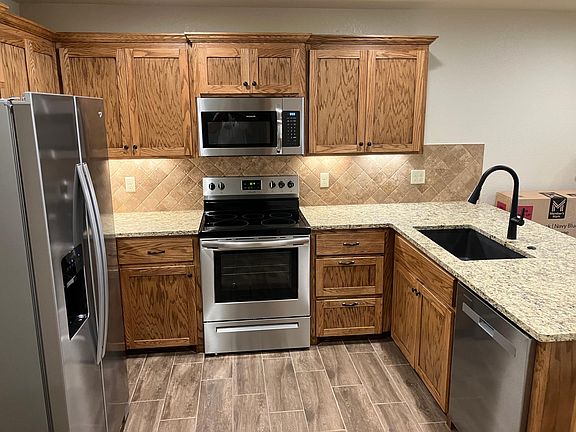 Stain grad oak cabinets, stainless steel appliances and lighted tumbled stone backsplash.