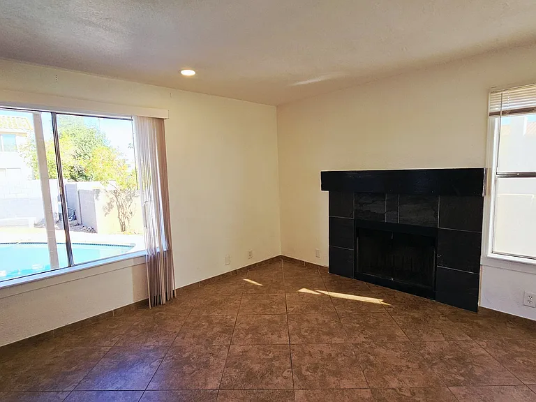 Bright and spacious living area featuring a cozy fireplace, large windows, and beautiful views of the backyard pool.