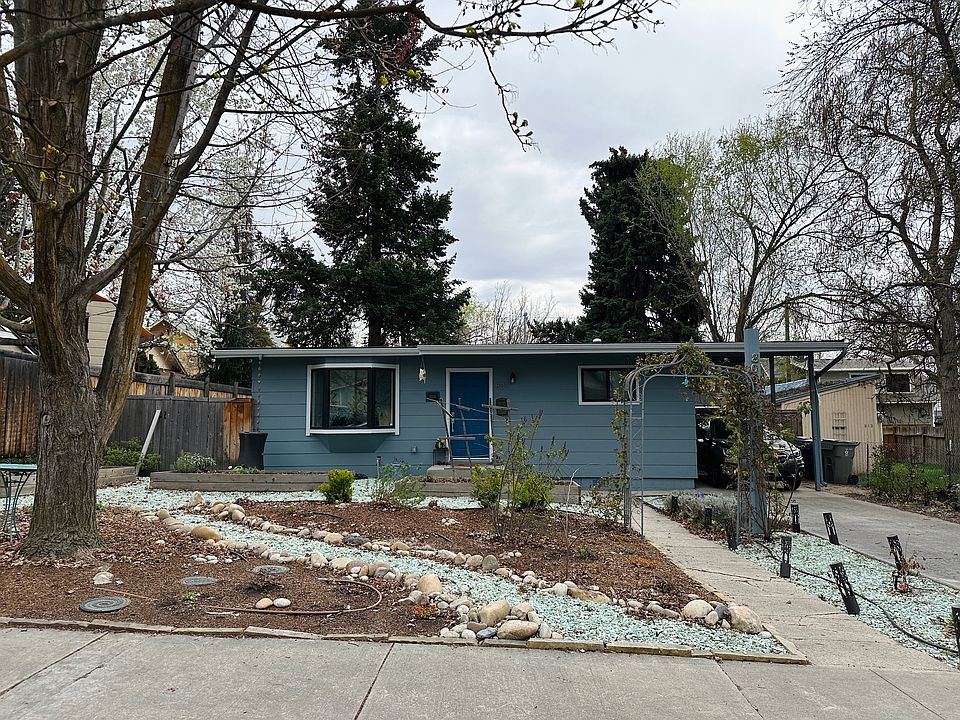 Front of the house with four raised beds. Includes carport and driveway. Can fit three cars