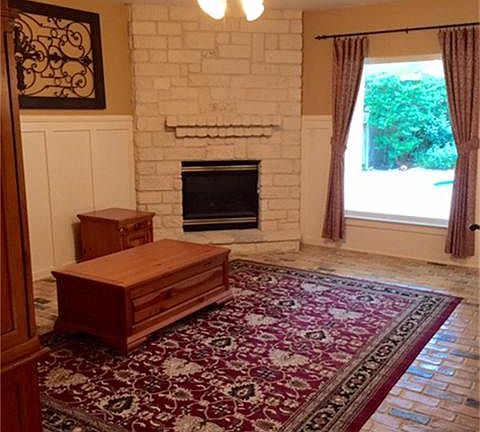 Warm and cozy den features limestone gas log fireplace perfect for cold days, large double pane window brings in outdoor view and natural light, brick flooring continues to flood throughout.
