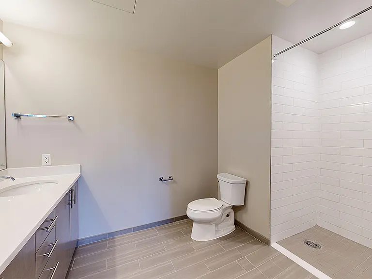 Apartment bathroom with glass-enclosed shower, wood-style flooring, and double sinks.
