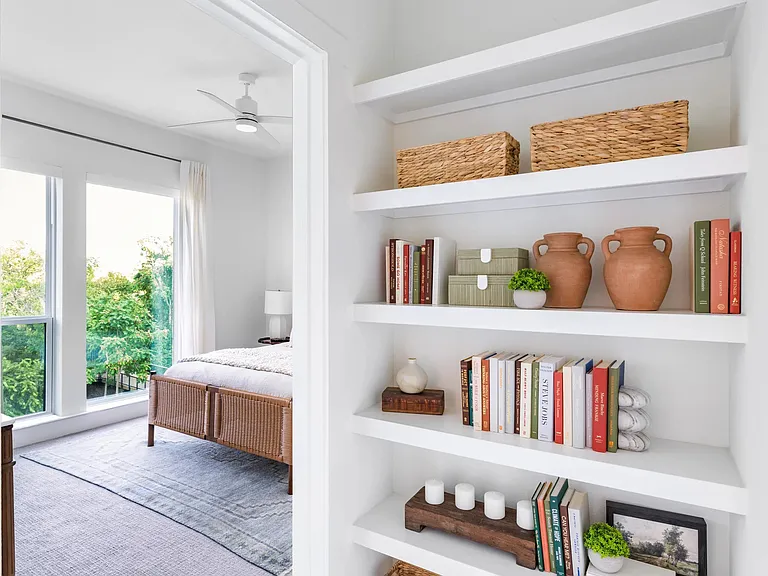 Built-in shelving with curated storage offers a thoughtful transition into a light-filled bedroom with open views and a calm, organized feel.