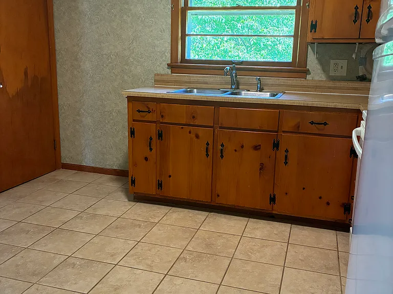 Additional kitchen view showing the tile flooring, wood cabinetry, and natural light from the window over the sink.