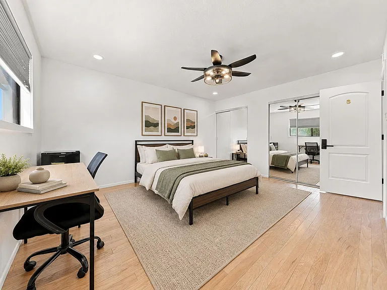 Spacious bedroom with a work desk, ceiling fan, and mirrored closet doors for ample storage and easy getting ready.