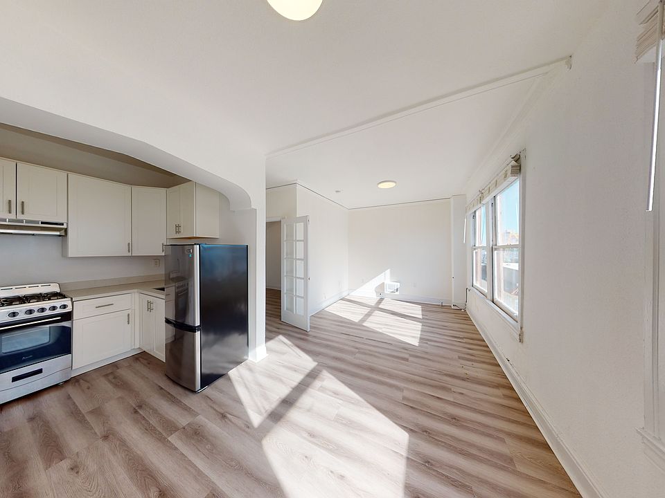 Spacious living room with a wood-like flooring, a view of the kitchen, and a large window offering natural light