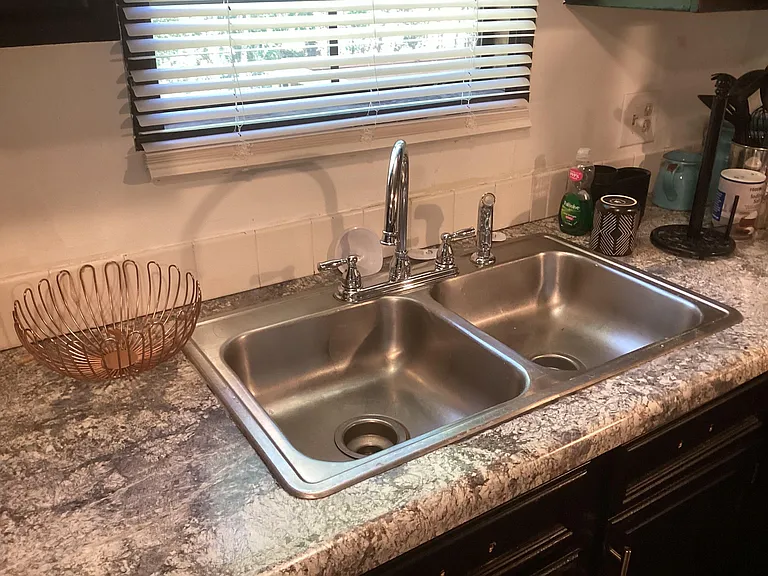 Double-basin stainless-steel sink with gooseneck faucet, laminate counters, and a window with blinds above the work area.
