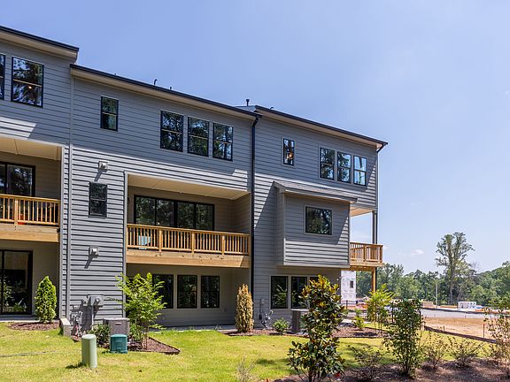 A multi-story residential building with wooden siding, balconies, and a grassy area in the foregroun