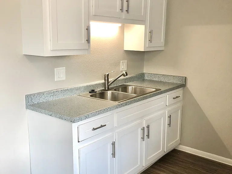 Modern kitchen space featuring sleek white cabinets, granite countertops, and a stainless steel sink with elegant fixtures.