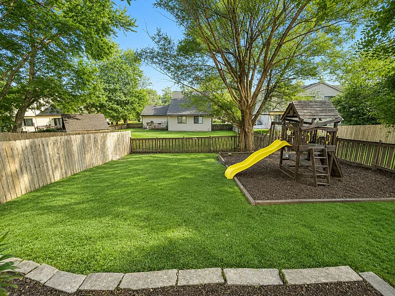 The generous backyard provides the perfect blend of recreation and relaxation, featuring a large lawn, mature trees for natural shade, and a children's play area that makes outdoor living both fun and functional.