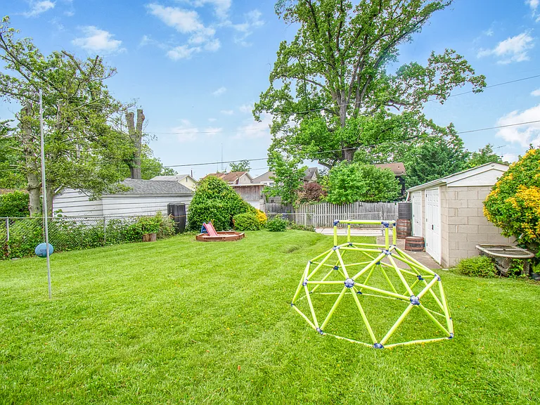 Back yard showing large storage shed with electricity, tether ball pole, climbing structure, and sandbox.