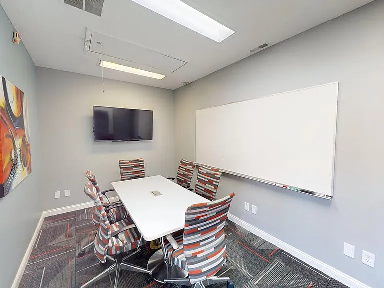 Contemporary meeting room featuring a sleek conference table, vibrant chairs, wall-mounted TV, and spacious whiteboard, ideal for productive gatherings.