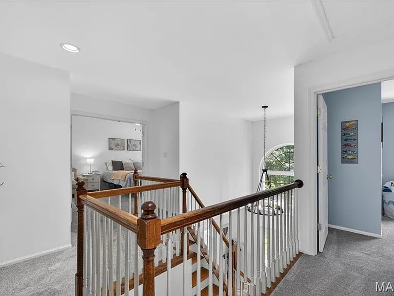 Upper-level landing featuring hardwood stair treads, a white spindle railing with wood handrails, and neutral carpeting