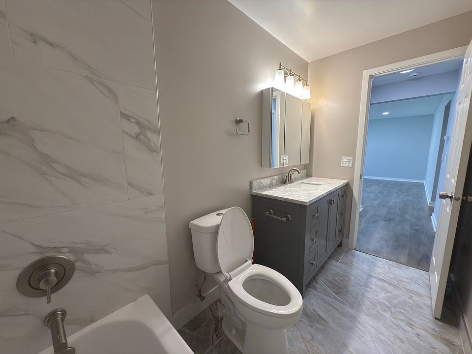 Modern fully remodeled bathroom featuring a sleek marble-look tile shower, updated vanity with stone countertop, and brushed nickel fixtures throughout.