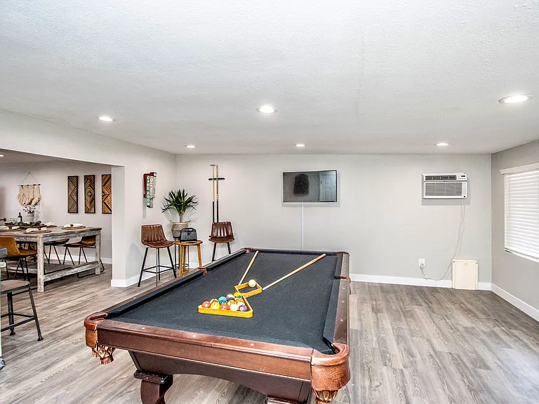 Fun game room at Casa Del Sol, Tempe rental home. Features a classic billiards pool table, mounted smart TV, bar seating, and AC unit, opening directly into the stylish dining area. Perfect entertainment space for a top Tempe, AZ corporate rental.
