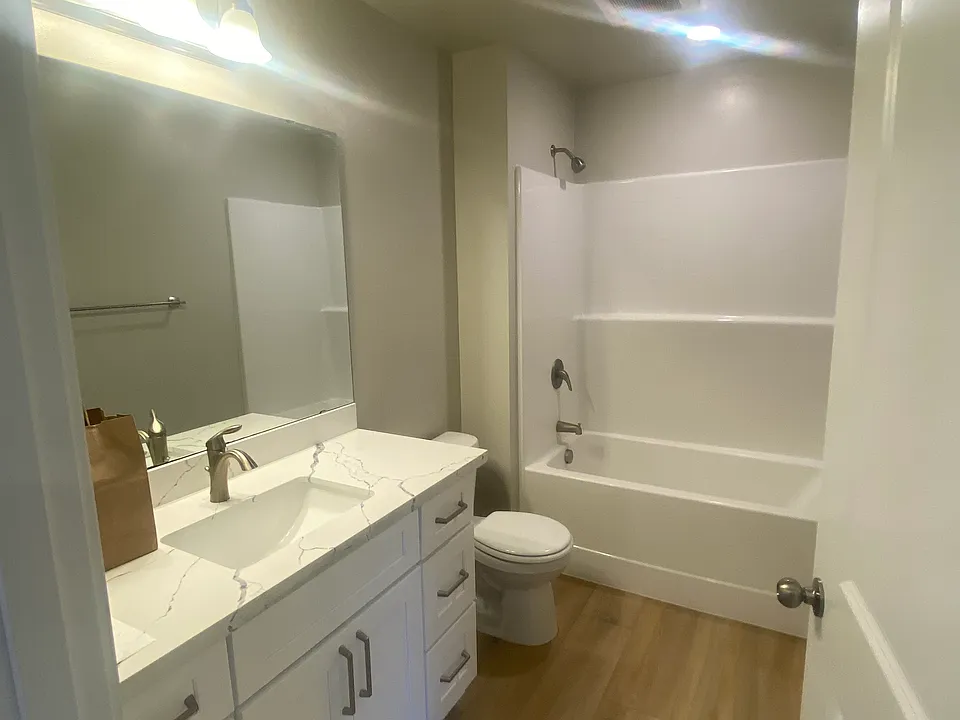 Well lit bathroom has matching quartz counter tops like kitchen. Soft close drawers and wide mirror share same design beauty on display the the kitchen space.
