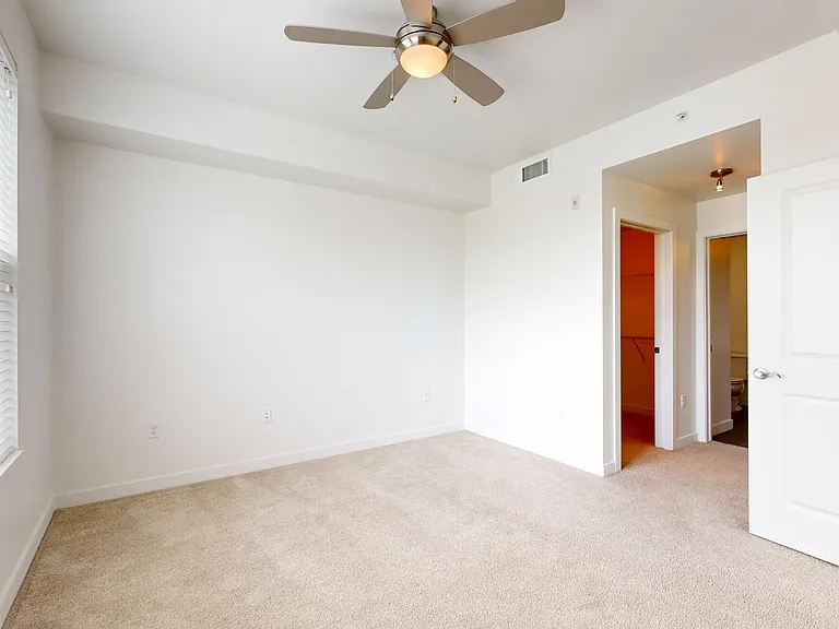 Spacious apartment bedroom with large closet, attached bathroom and plush carpet flooring.