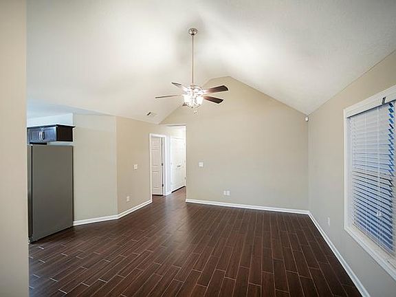 Open living room with porcelain tile floors. Vaulted ceiling and two inch faux wood blinds