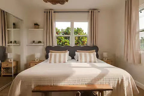 Inviting bedroom with a queen-sized bed and soft linens. Sunlight fills the room, and bedside lamps add warmth and a stylish, relaxed vibe.