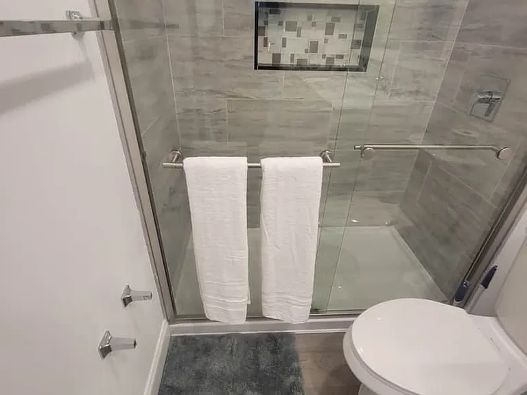 Modern tiled shower with glass door, bath mat, towels, and towel racks available.