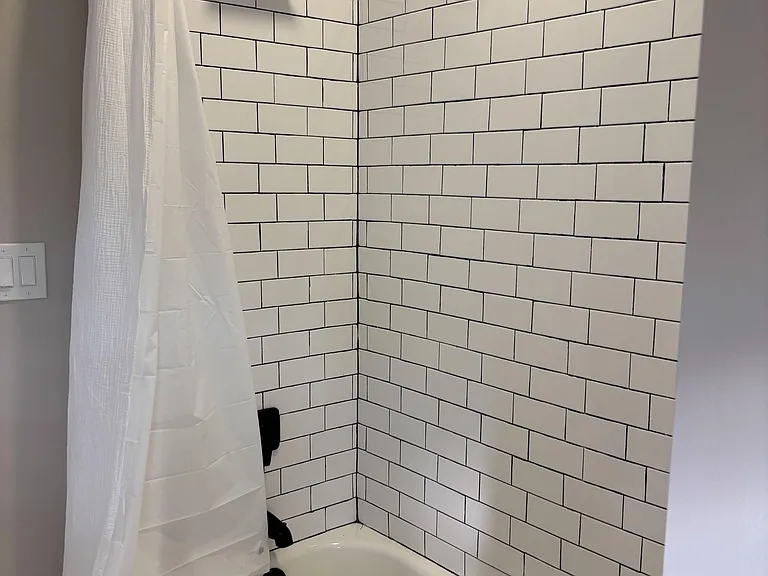 Tub/shower combo with classic white subway tile surround, matte black fixtures, and a clean, simple shower curtain.