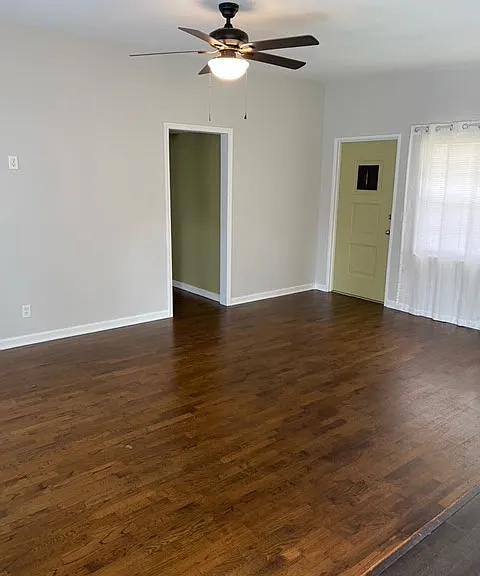 Inside view hardwood floors in living room, and front door. Hallway leads to bedrooms and bathrooms.