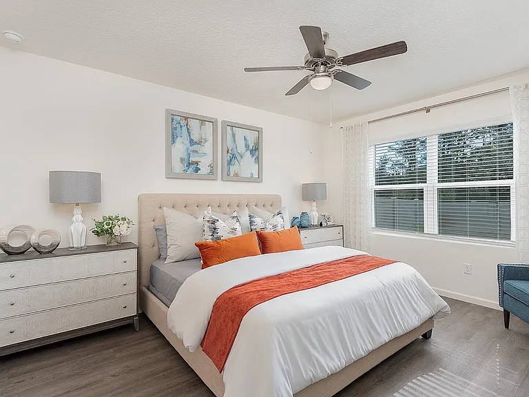 Bright and inviting bedroom with modern decor, featuring a plush bed with vibrant pillows, elegant bedside lamps, and large windows letting in natural light.